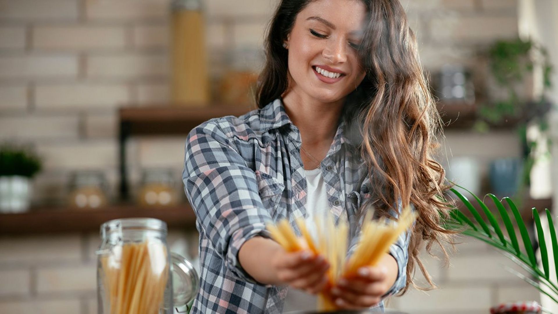 Lächende Frau in kariertem Hemd hält Spaghetti in der Küche Lächende Frau in kariertem Hemd hält Spaghetti in der Küche