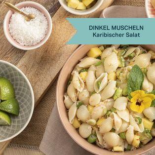 Schüssel mit DINKEL MAX Muscheln und karibischem Salat, umgeben von Zutaten wie Limetten und Gewürzen auf Holzuntergrund