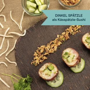 Dinkel Spätzle mit Käsespätzle-Sushi, angerichtet auf dunklem Untergrund mit Kräutern und Gewürzen