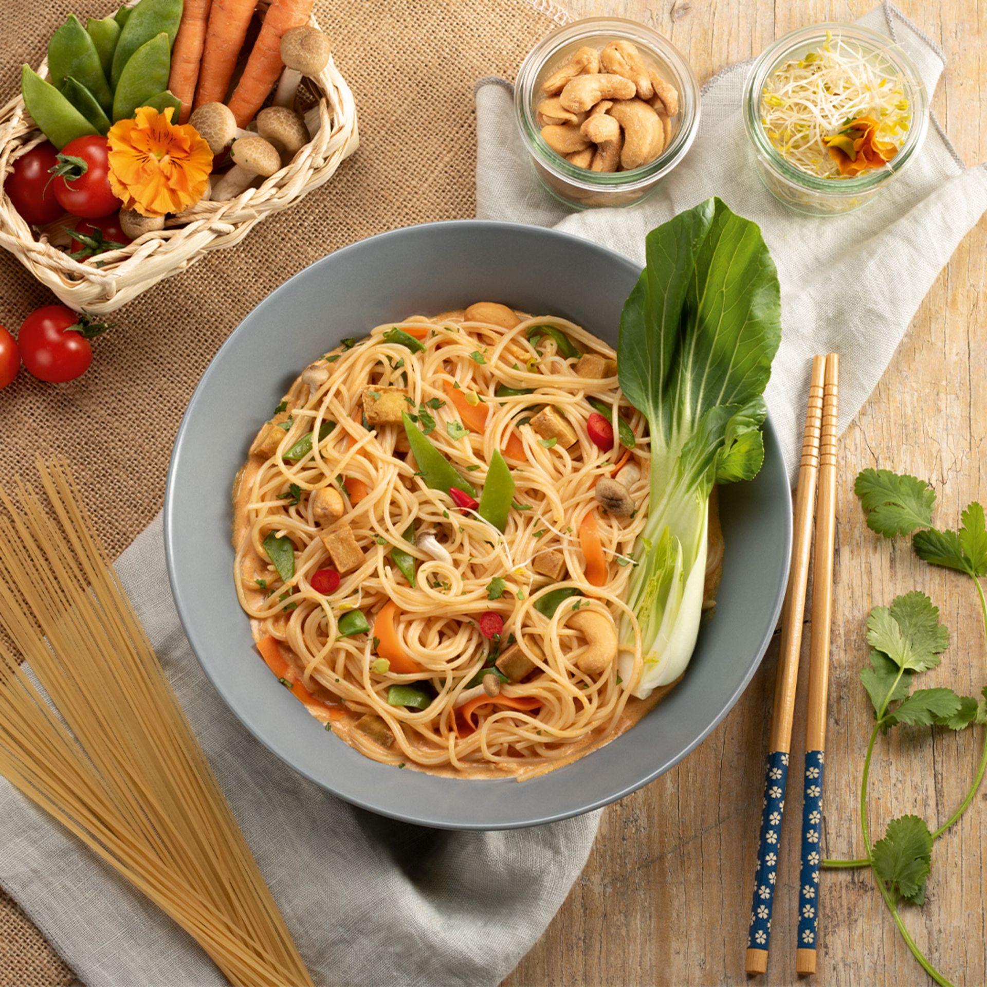 Spaghettini mit Tomatensauce, Garnelen und Kräutern auf einem grauen Teller, umgeben von frischen Zutaten und Gewürzen