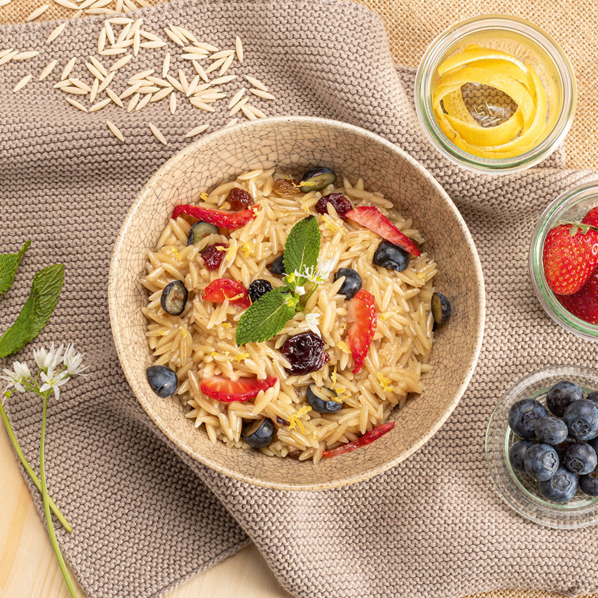 Schüssel mit Nudelreis, Blaubeeren und Minzblättern auf einem Tisch mit weiteren Zutaten wie Blaubeeren und Öl